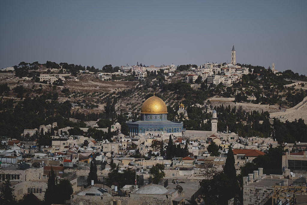 A blue and gold domed mosque sits surrounded by old stone buildings of a city.