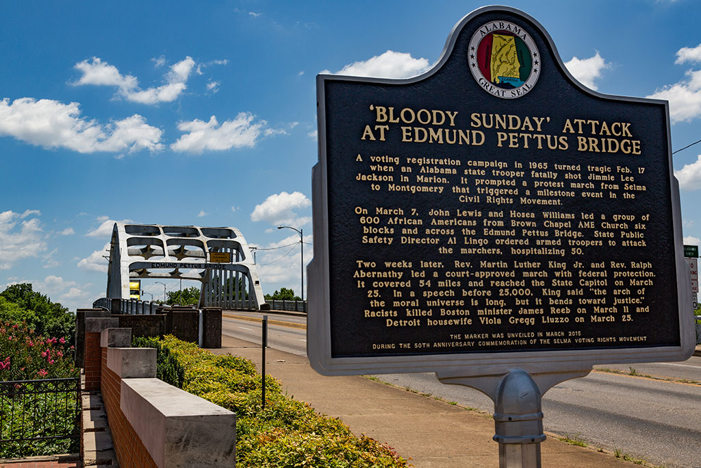 A history interpration sign stands by the highway approach to a arched bridge.