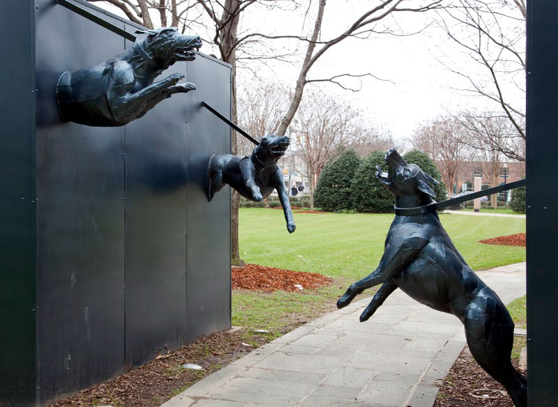 a path passes between two monoliths from which sculpted aggressive dogs emerge.