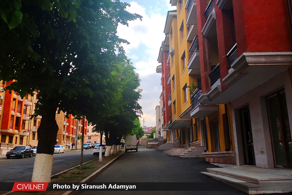 An avenue of colourful flats beside green trees.