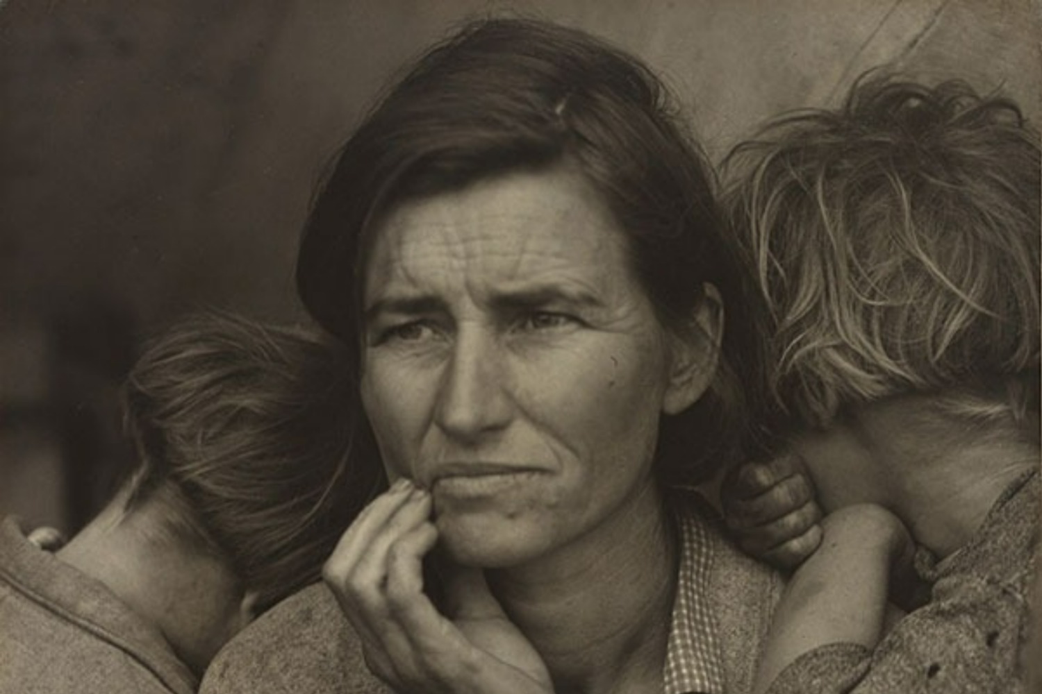 A black and white close up of a mothers cradling her jaw in worry as children cuddle into her.