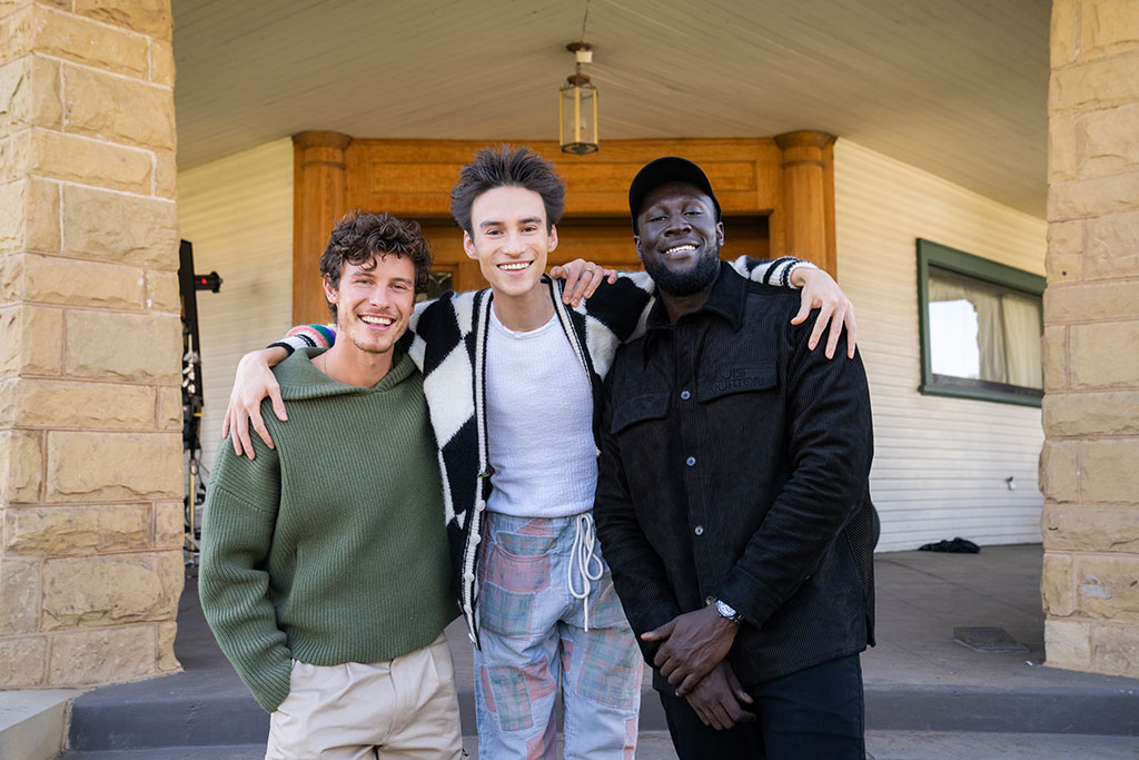 Three happy men stand with the one in the middle draping his arms around his friends.