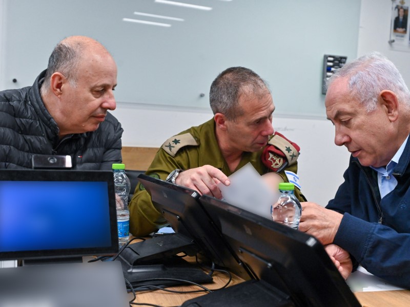 Three men huddle around a laptop and talk animatedly.