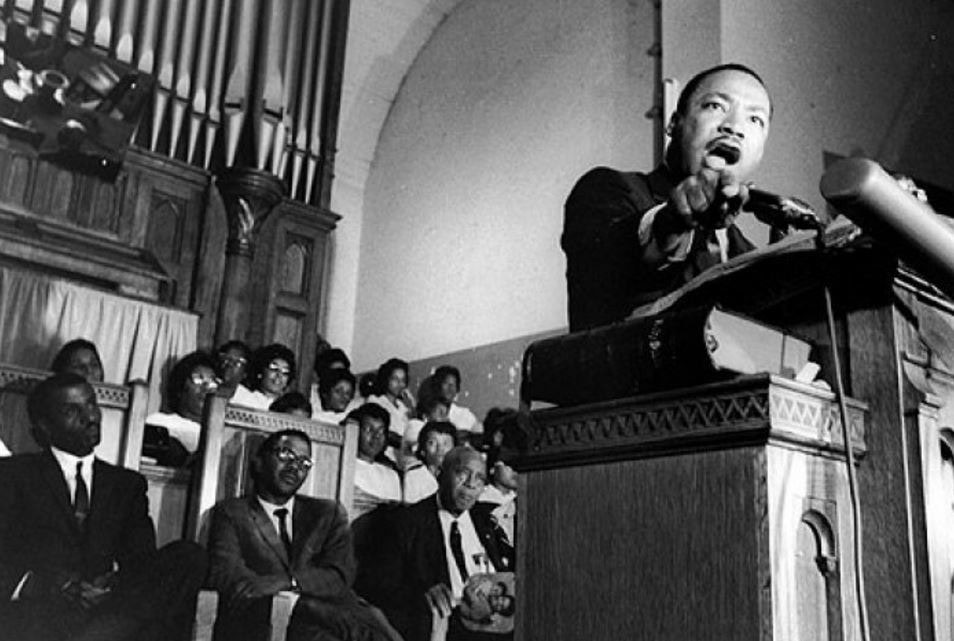 Martin Luther King reaches from the pulpit of a church while he preaches.