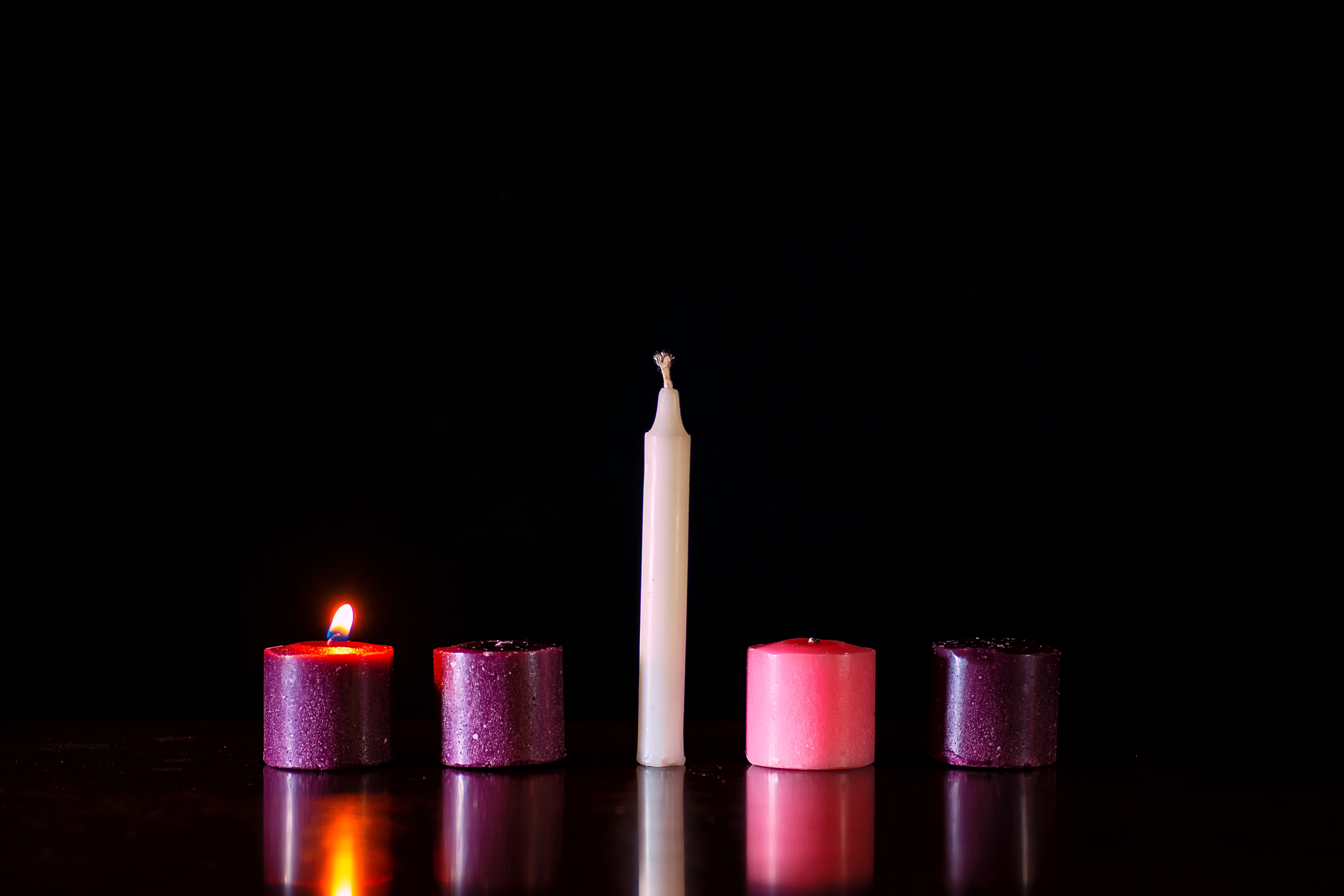 Five candles sit in a row against a dark background, only one is lit.