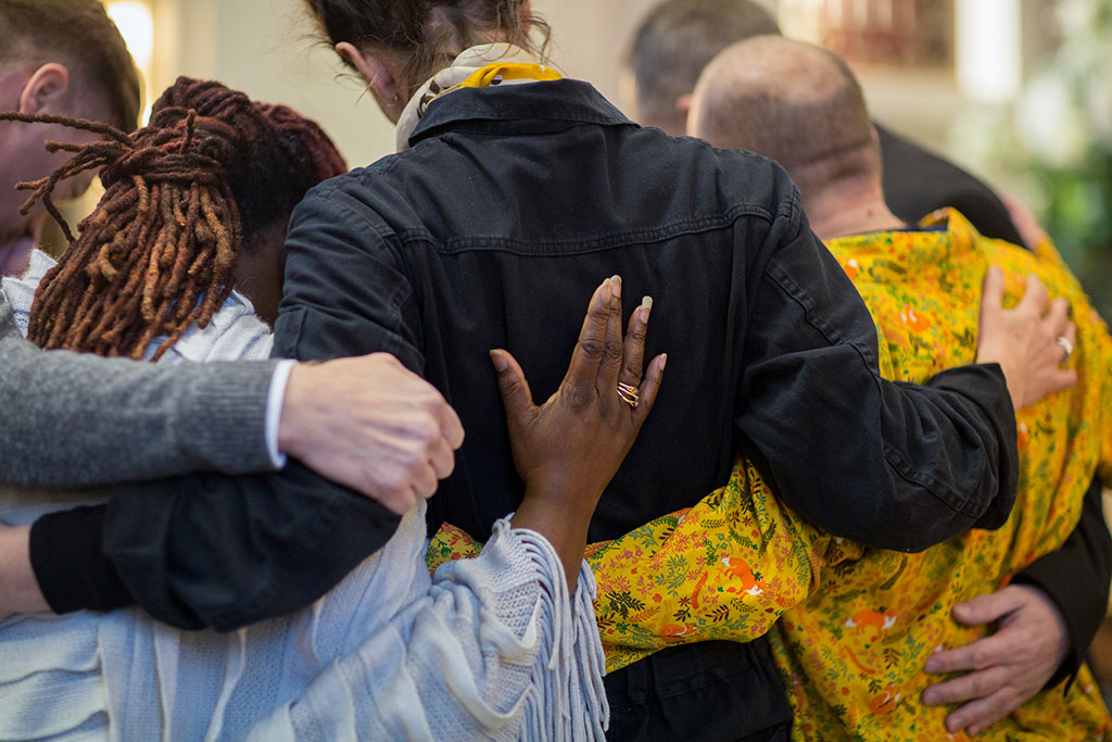 A group of grieving friends with their hands on each others backs.