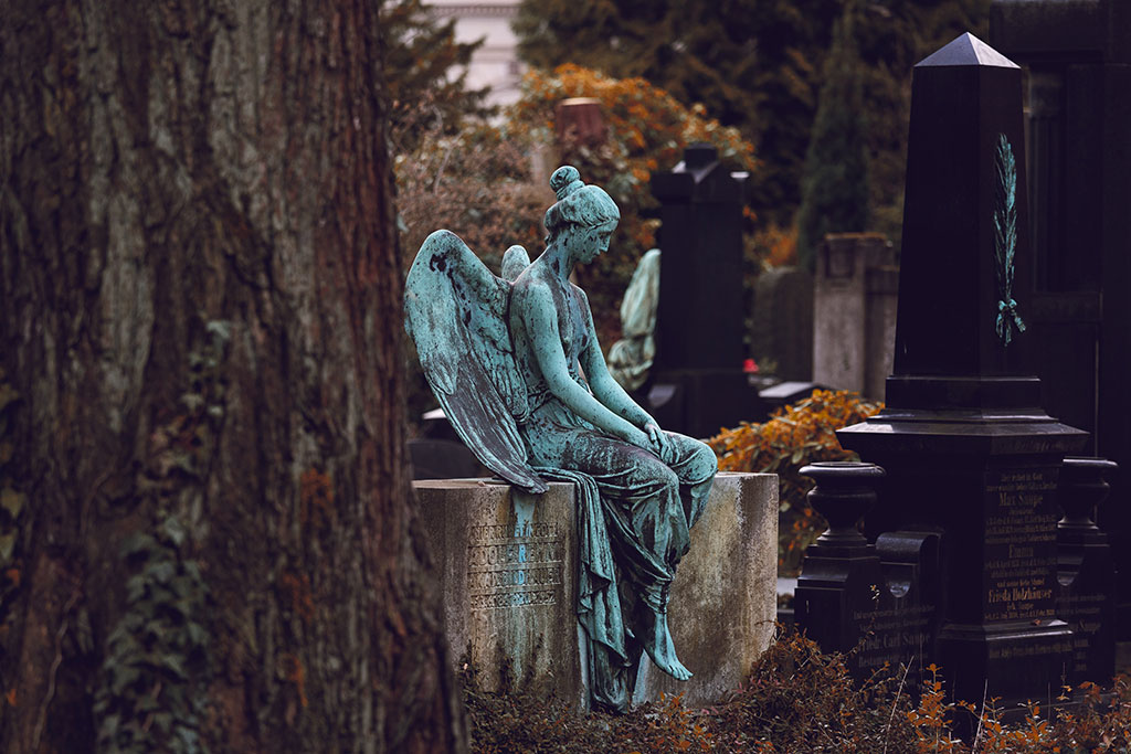 A bronze statue of a resting angel sits atop a low stone grave.