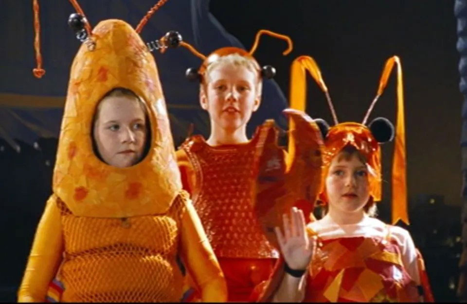 Three children dressed as orange lobsters stand sheepishly on a stage.