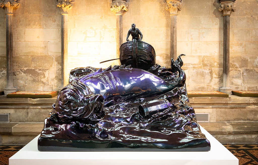 A bronze sculpture of a small boat and sea monster tossed in the waves.