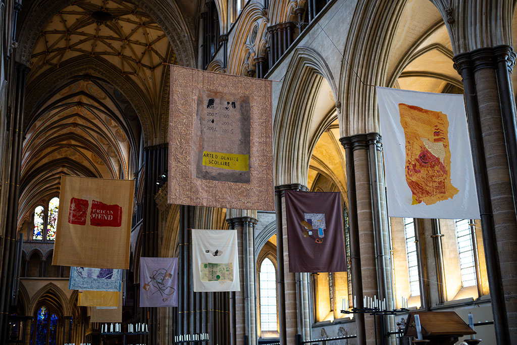 Artistic banners are hung high above the nave of a cathedral between pillars and arches.