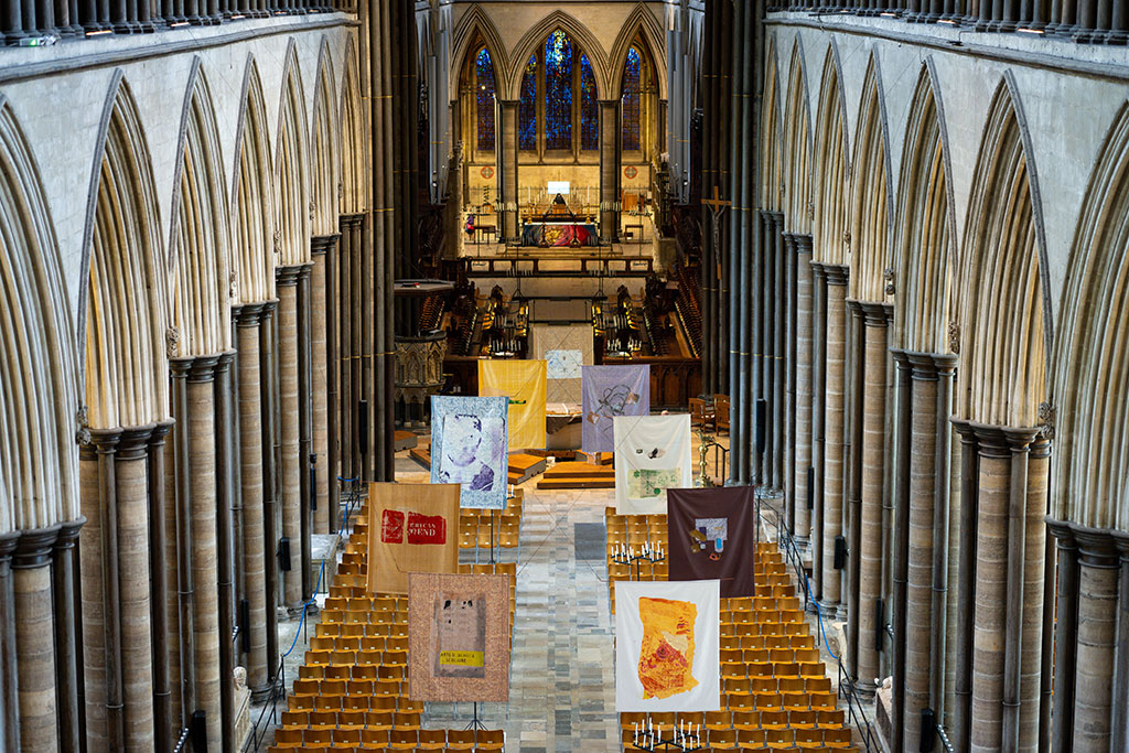 Artistic banners are hung high above the nave of a cathedral between pillars and arches.