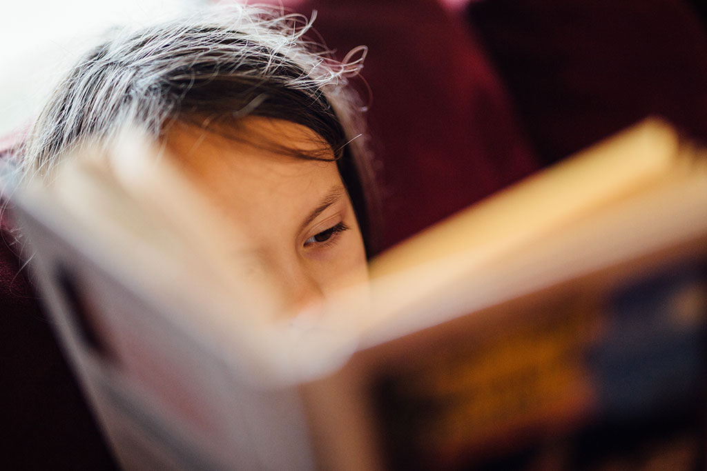 A close up of face, showing an eye, mostly obscured by a closely-held open book.