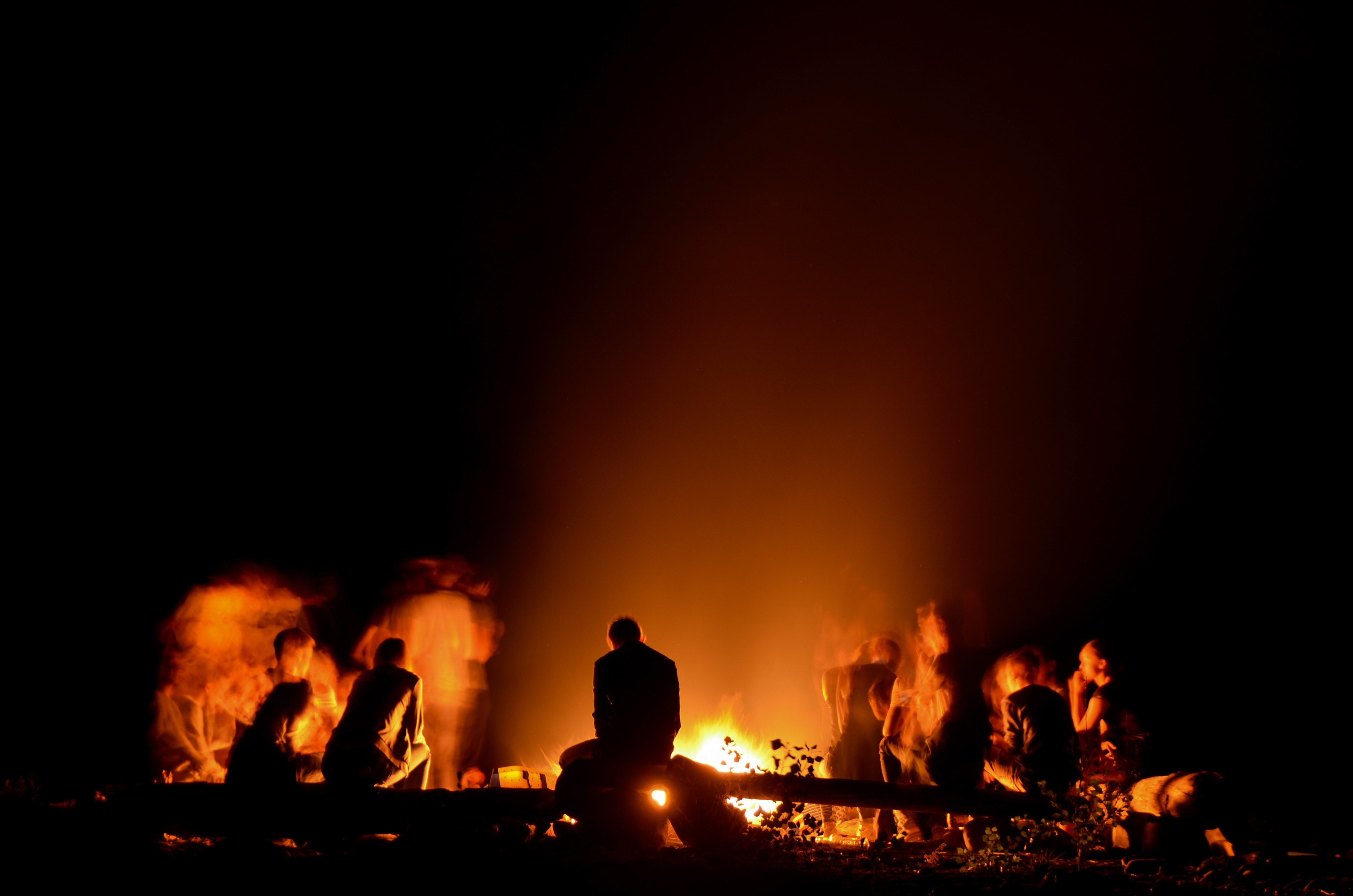 People sitting around a campfire are silhouetted against the night.