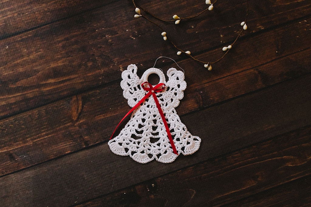 A white crocheted angel decoration against a dark background.