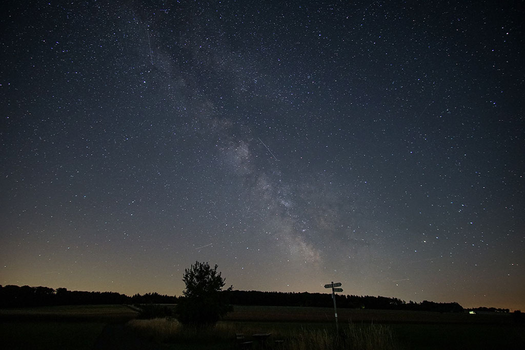 A starry night sky below which a signpost is silhouetted.