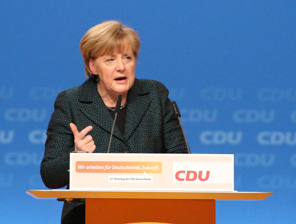 A politician stands a labelled lectern speaking and gesticulating with a hand.