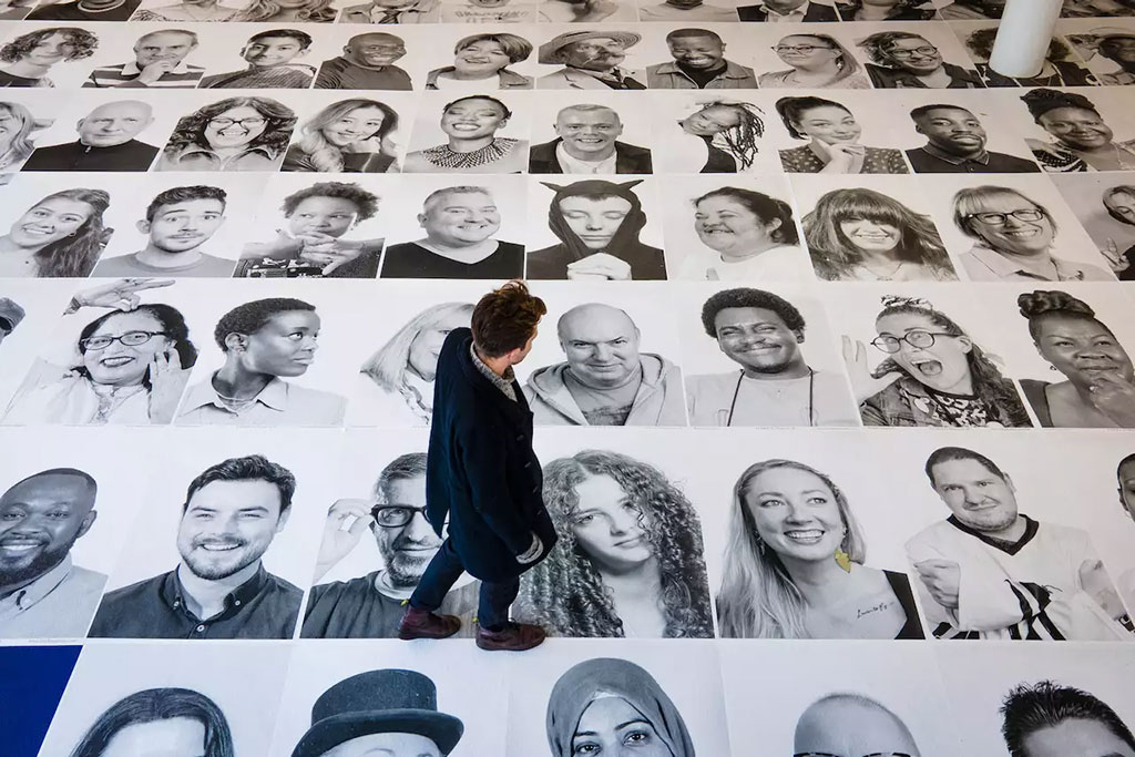 Looking down on a man walking across a grid of large black and white portrait photographs of people's faces