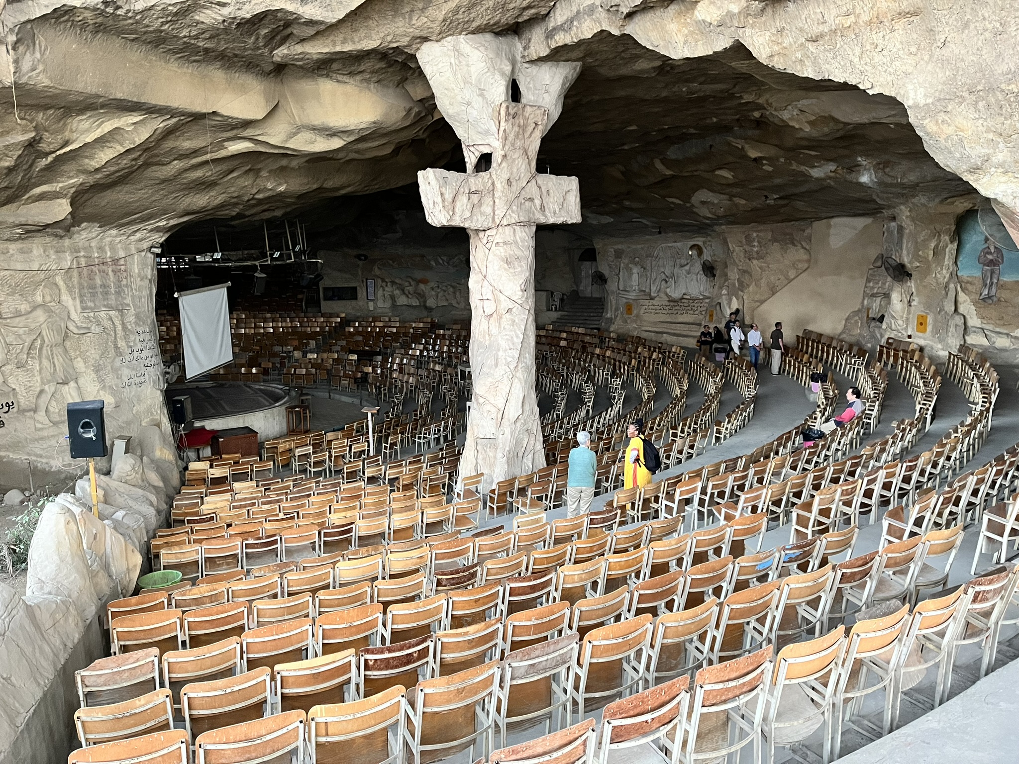 A church amphitheatre within a cave with a carved cross on a supporting pillar.