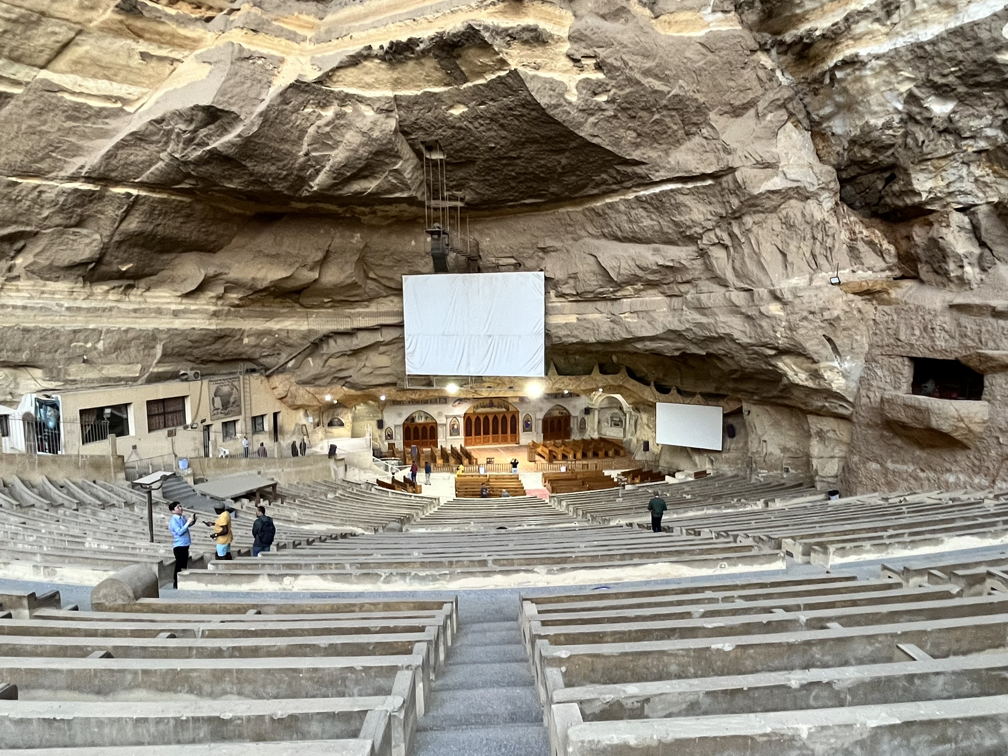 A screen dominates the centre of a church in a cave with amphitheatre seating.