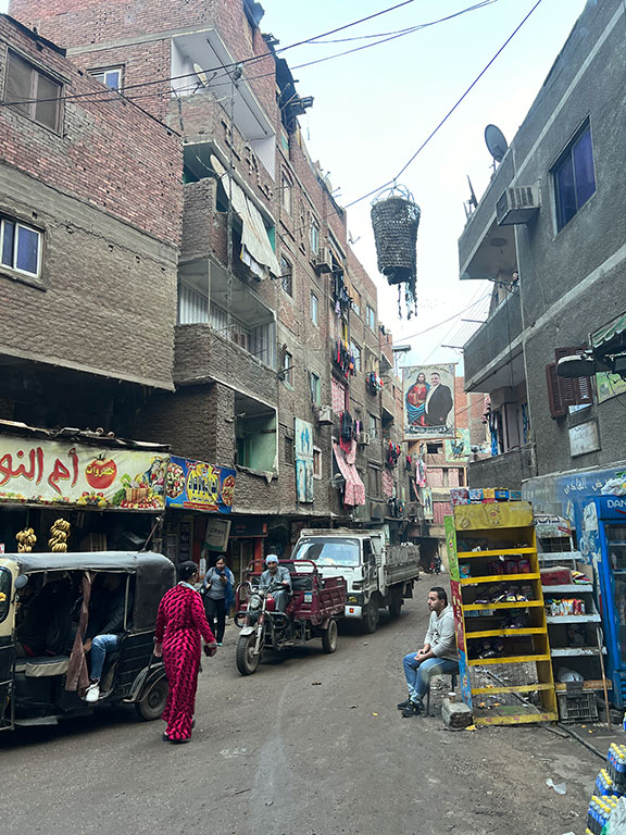 A suspended basket hangs above a narrow, rubbish strewn street.