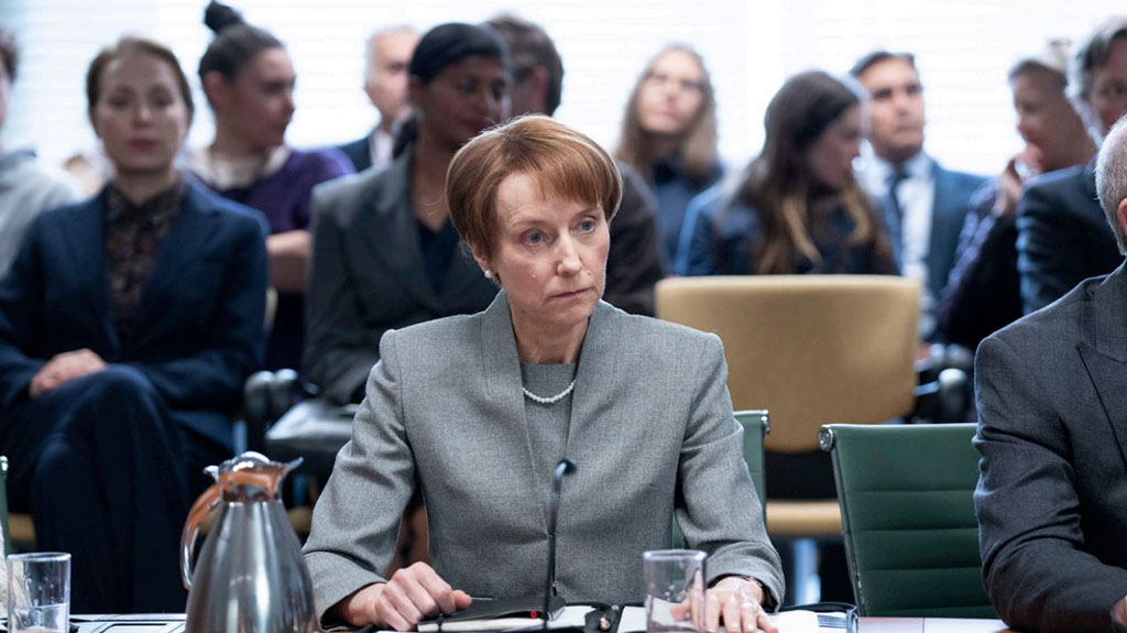 A tense-looking woman, sitting at  desk, stares into the middle disance.