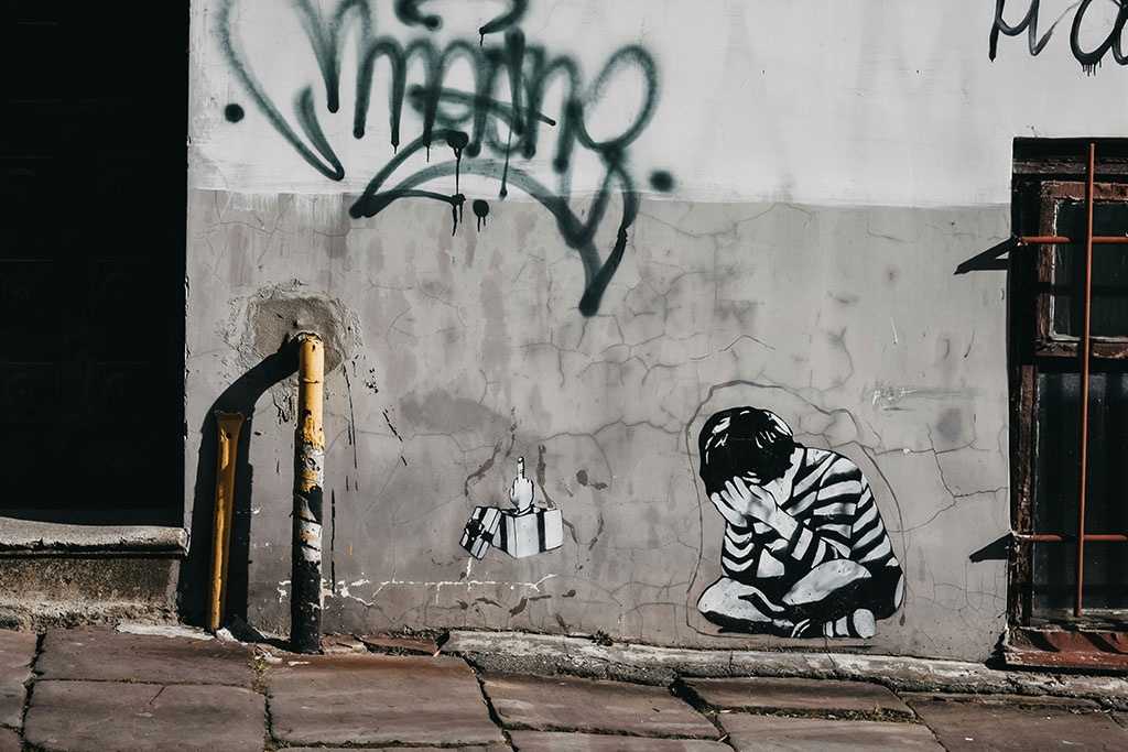 A grey and white wall graffited with a tag a image of a person crumpled and crying.