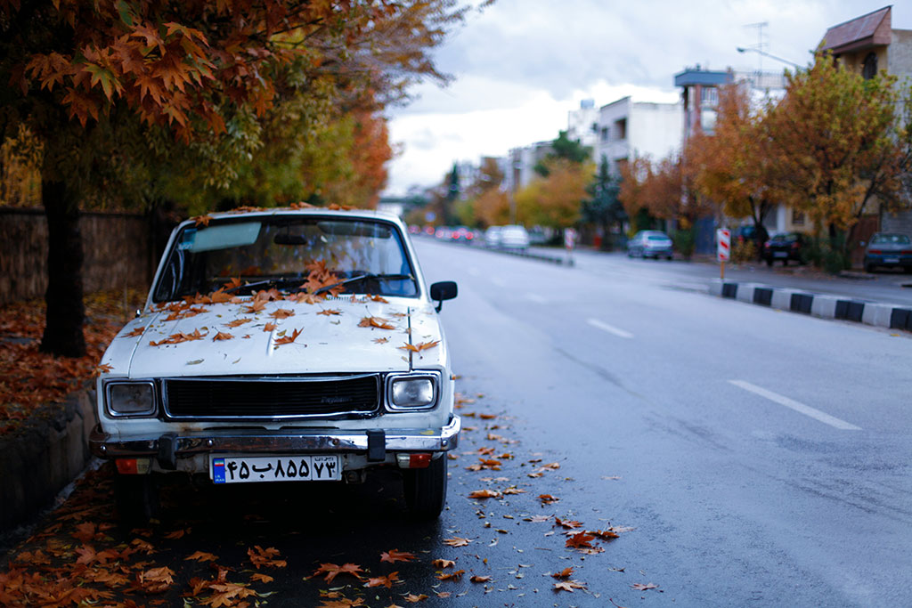 A somewat beaten white car parked on the side of a street.