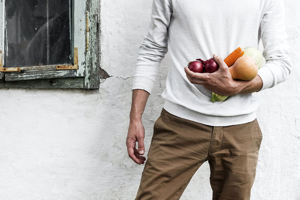 A man stands at rest, one arm holding some vegetables.