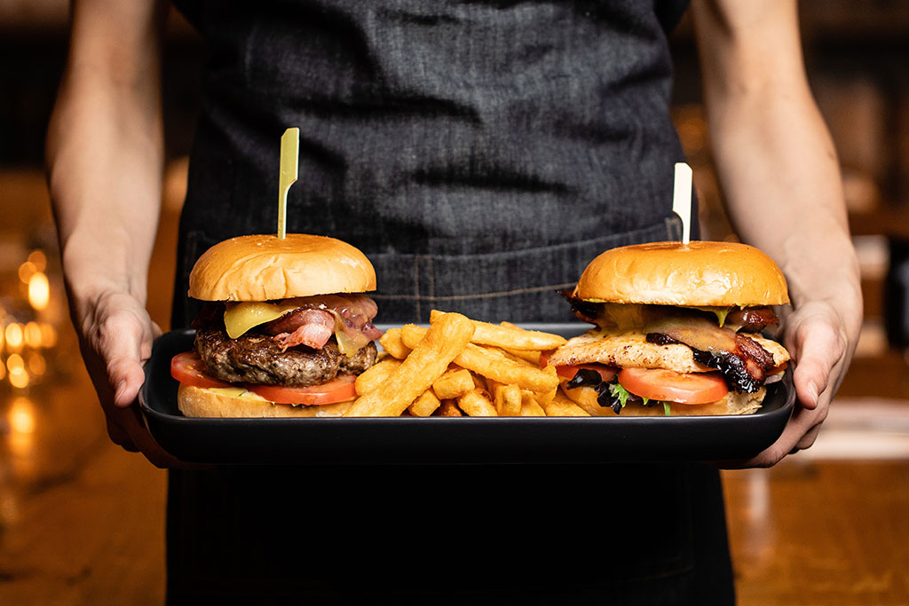 Two stuffed cheeseburgers are carried on a tray.