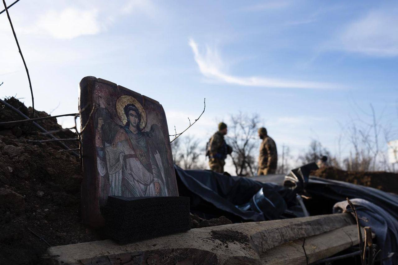 A religious icon is propped on the side of a trench, a soldier can be seen further down the trench.