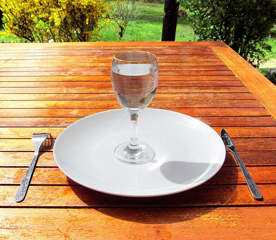 A wine glass of water sits on an empty clean plate.