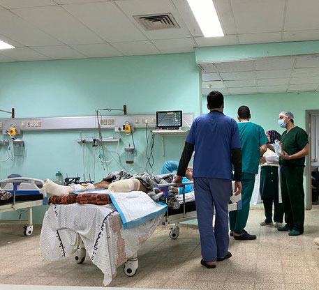 Medical staff stand beside a bed in which a man lies with an amputated leg.