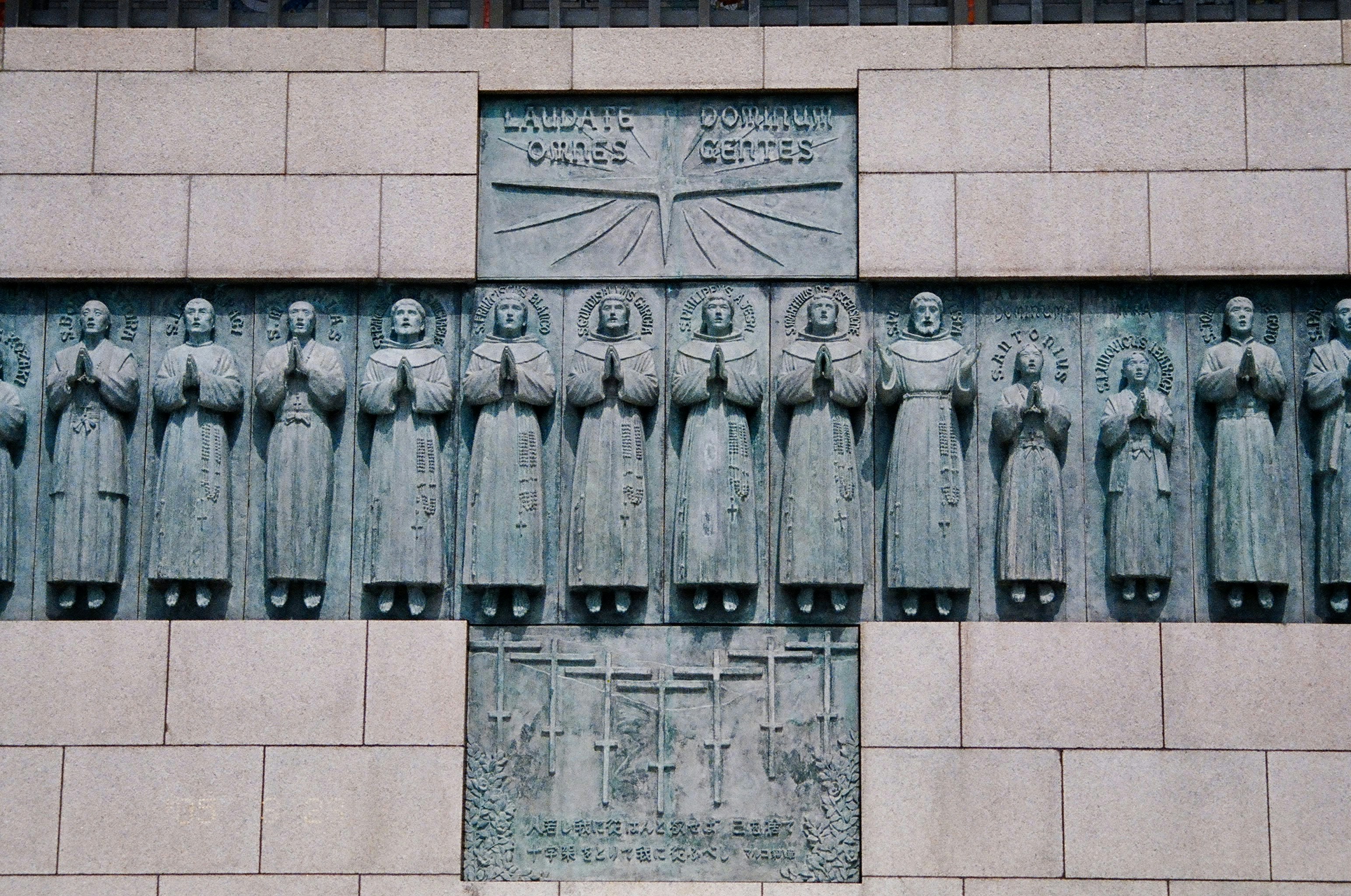 A stone monument within which set, in the shape of a cross are statues of numerous standing praying figures.