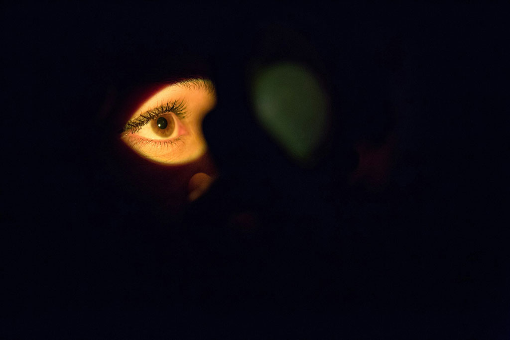 From a darkly shadowed face, a single illuminated eye stares.