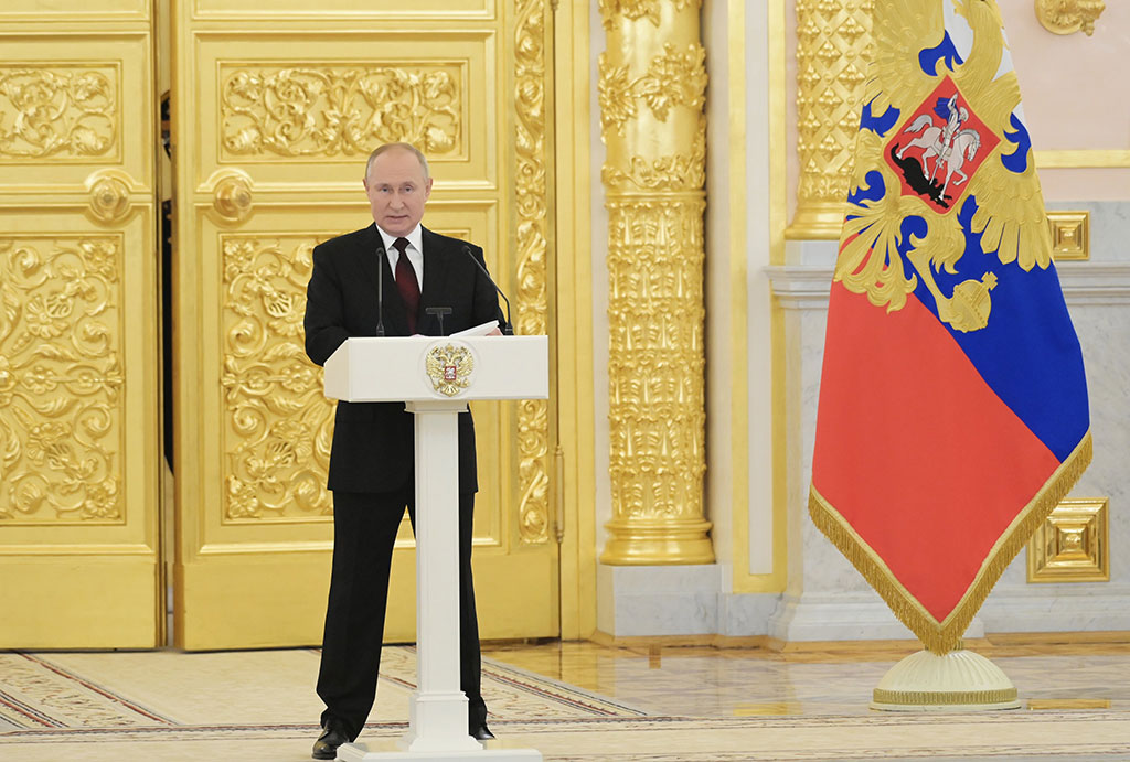 Preisdent Putin stands behind a lectern with a gold door and Russian flag behind him.