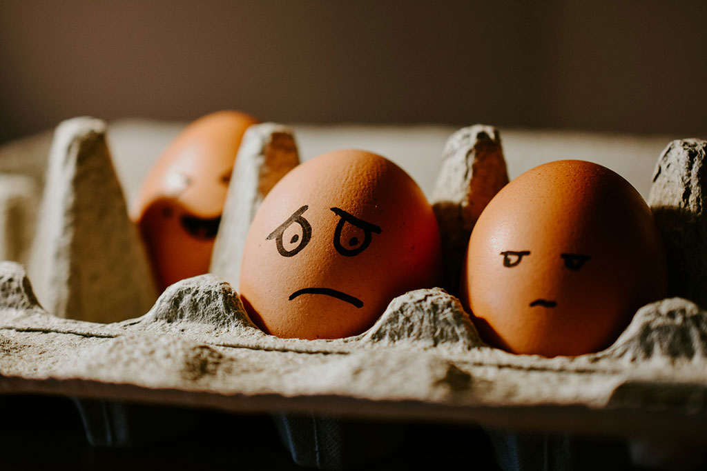 In an egg box sit two eggs with faces drawn on them with marker pen. One looks worried, the other looks on.