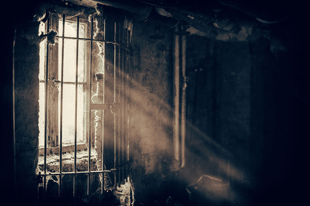 A window sheds light through locked bars into a dusty and dark room,