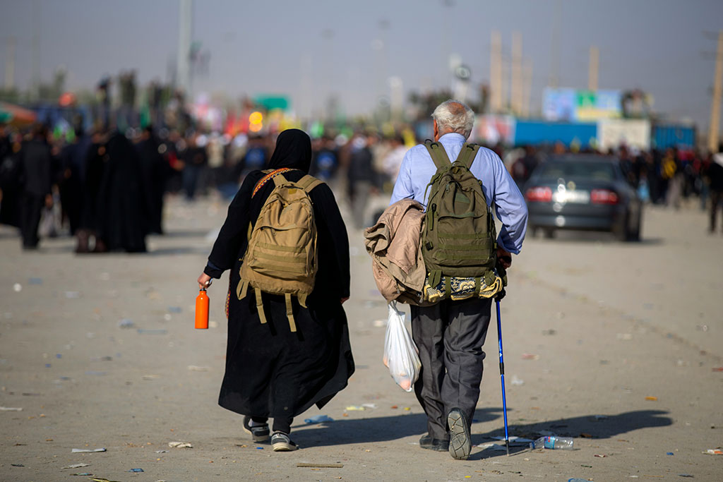 An elderly couple with rucsacks walk along a dusty road on pilgrimage