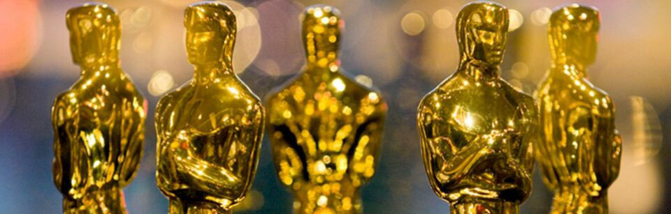A closely cropped group of gold Oscar statues showing mostly their head and shoulders.
