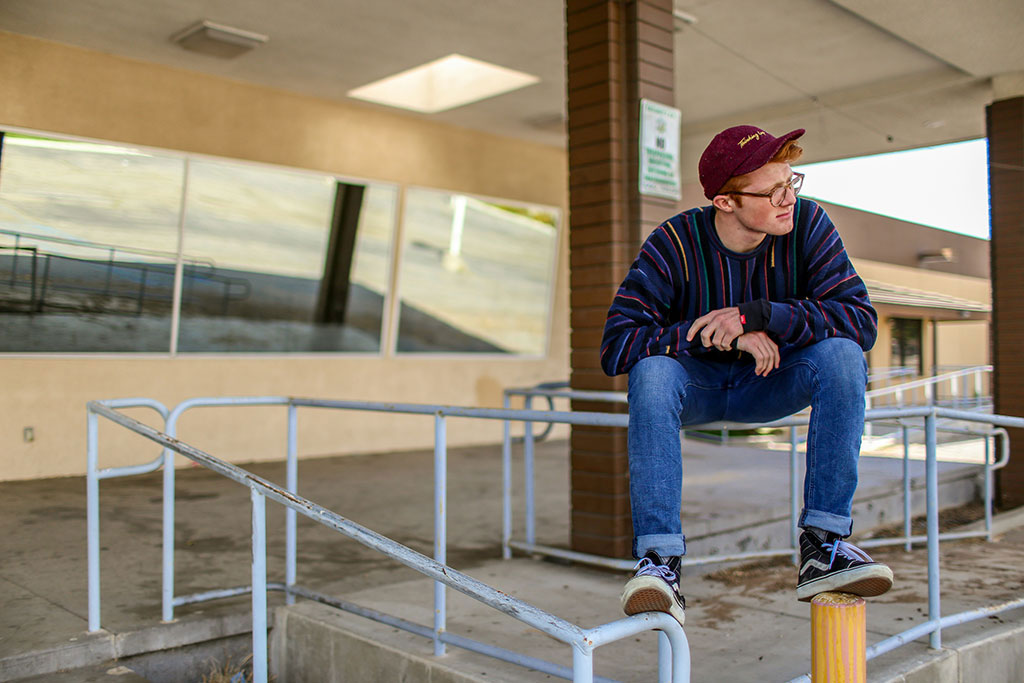 A casually dressed man perches on railing balancing, clasping his hands and looking around.