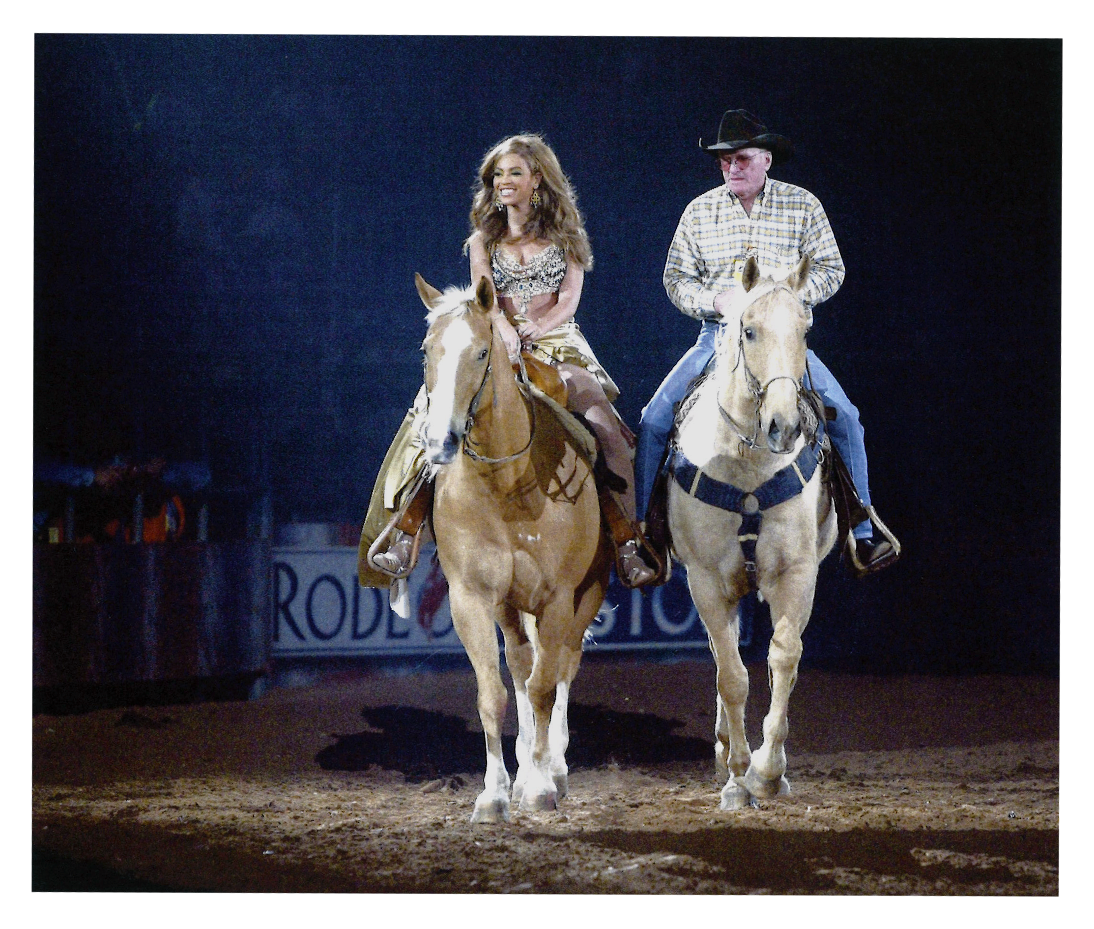 Side by side, two rodeo riders on horses trot toward the camera. One is Beyonce, the other a cowboy