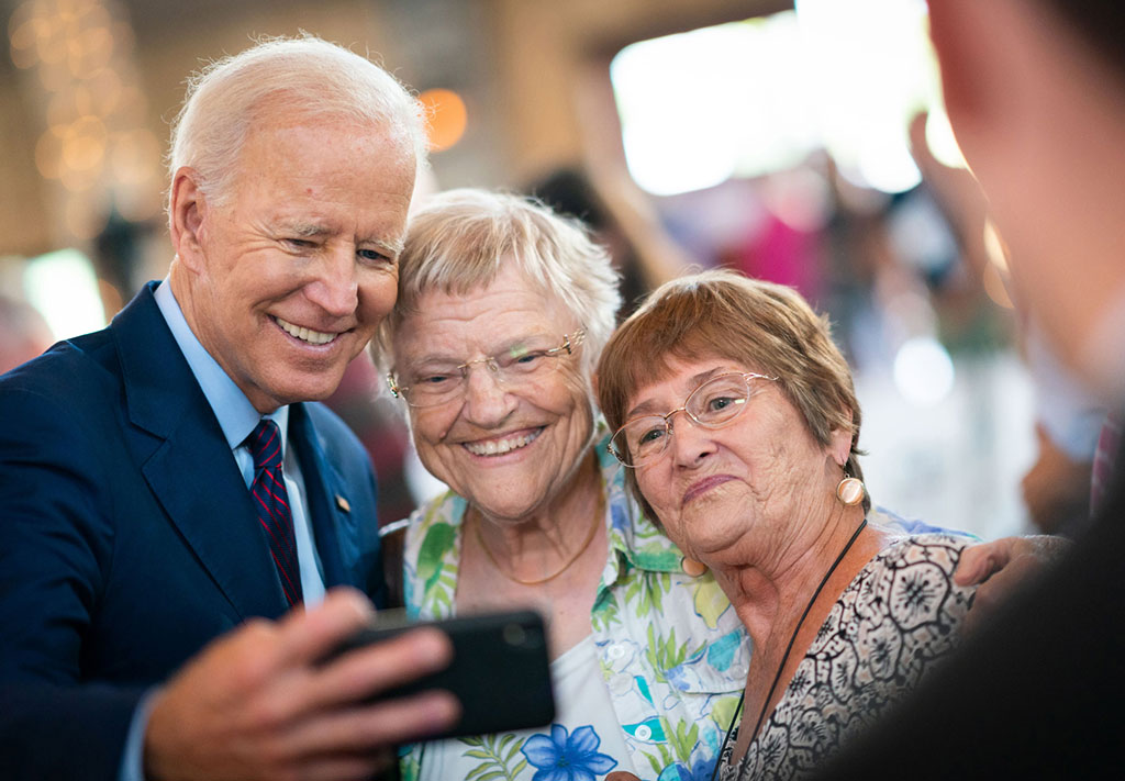 Joe Biden holds a phone as two supporters crowd in for a selfie