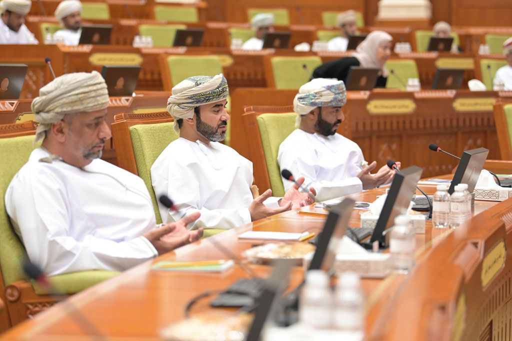 Three members of the Oman Shura sit in it's chamber and hold their hands in prayer