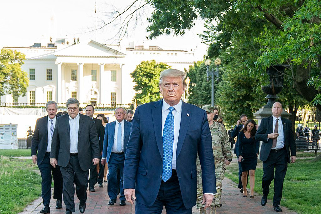 A fierce looking man walks at the head of a phalanx of suited men.