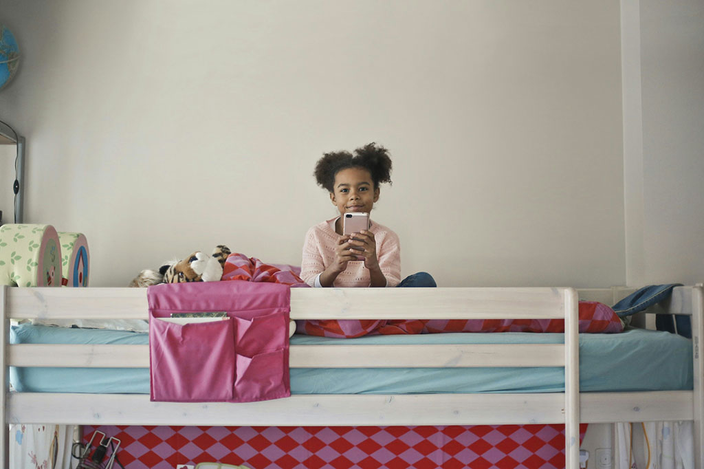 A child sits atop a bunk bed holding a phone in front.