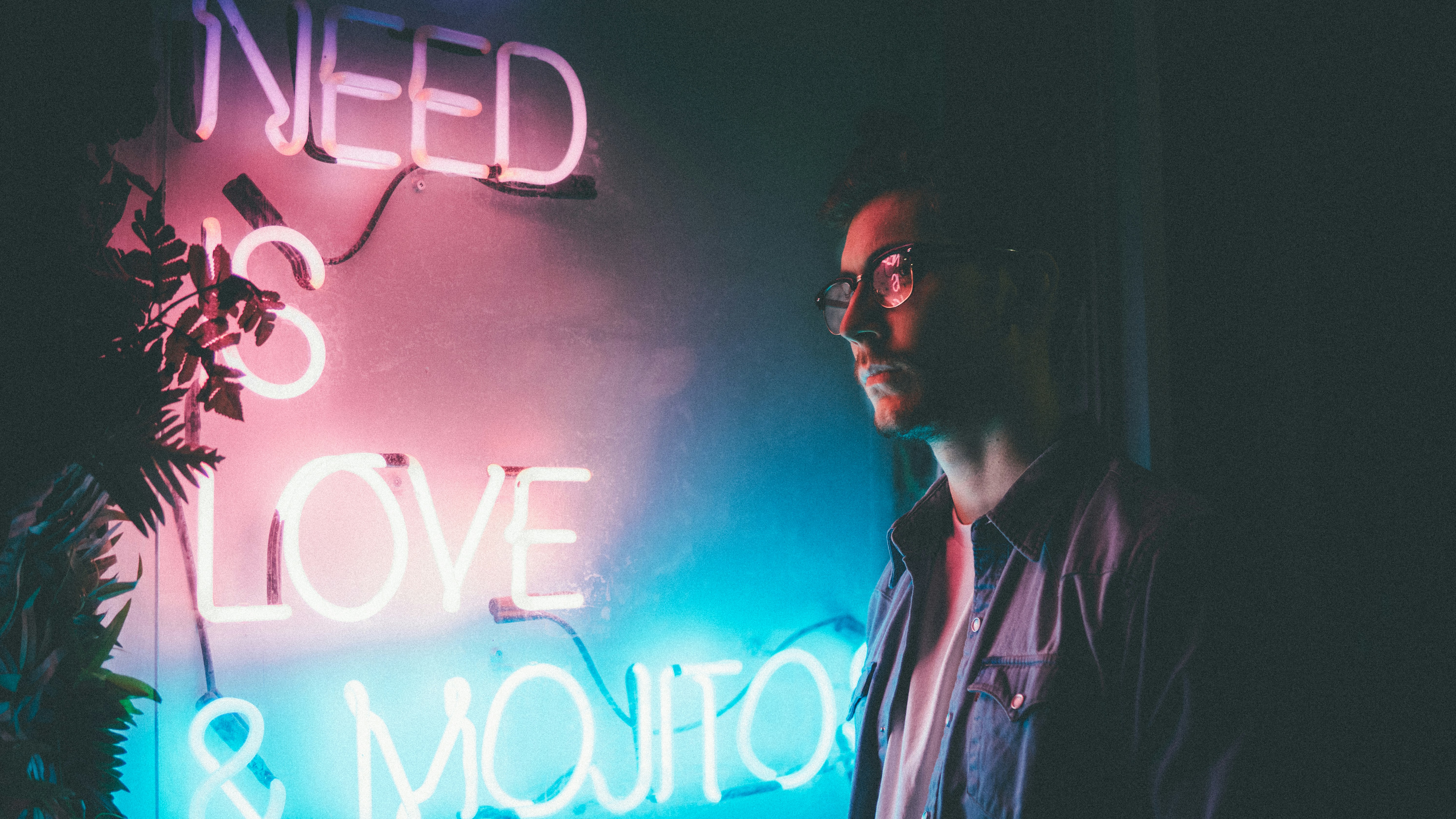 A man stands and looks at a neon sign reading 'need love and... '