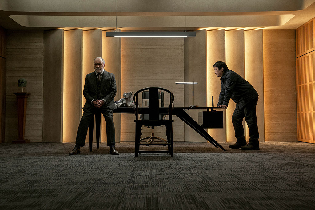 a man leans against one end of a table one another sits against its other end.