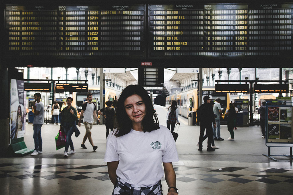 A young person stands in front of railway station platfrorms and below a large informaton display.