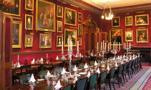 A grand dinner table set for a meal sits within a large room with paintings on the wall.