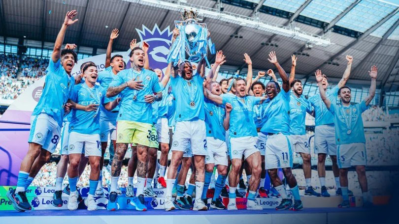 A football team wearing a sky blue kit leaps for joy holding a trophy.